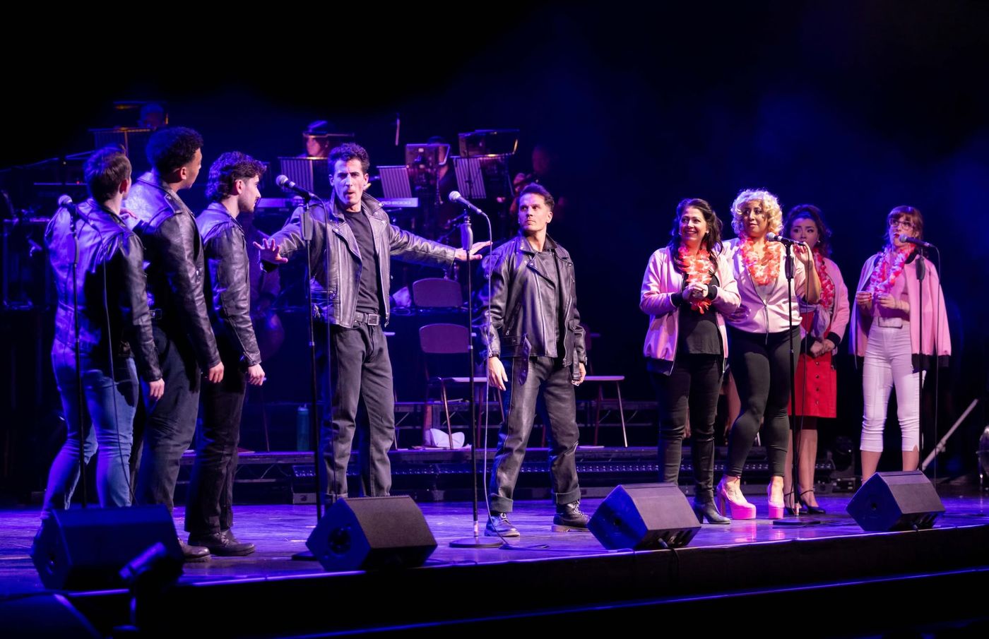A line of performers in leather jackets with arms outstretched