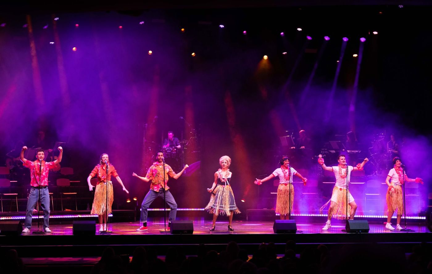 The company spread across the stage in pink light