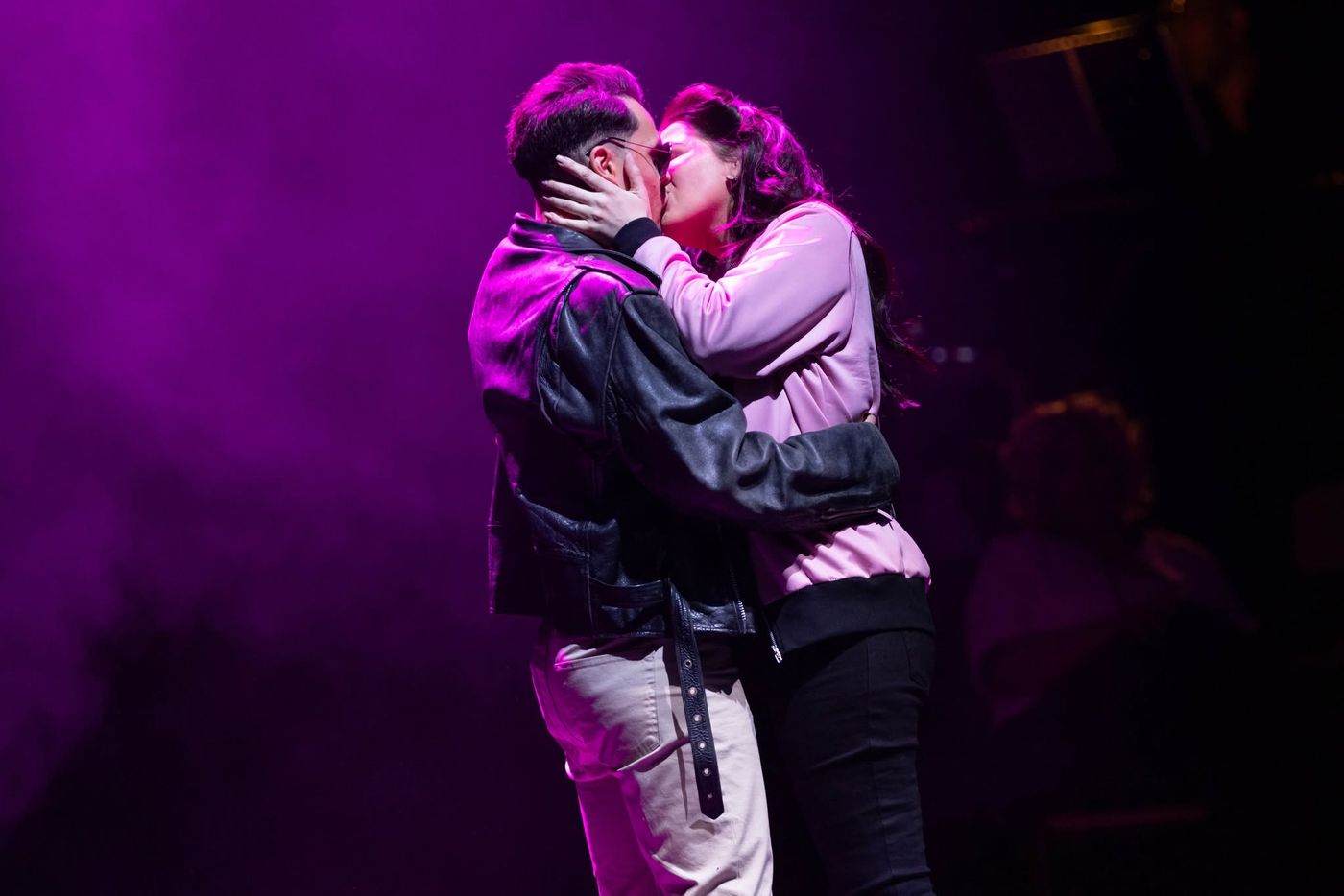 Two performers embracing under pink light