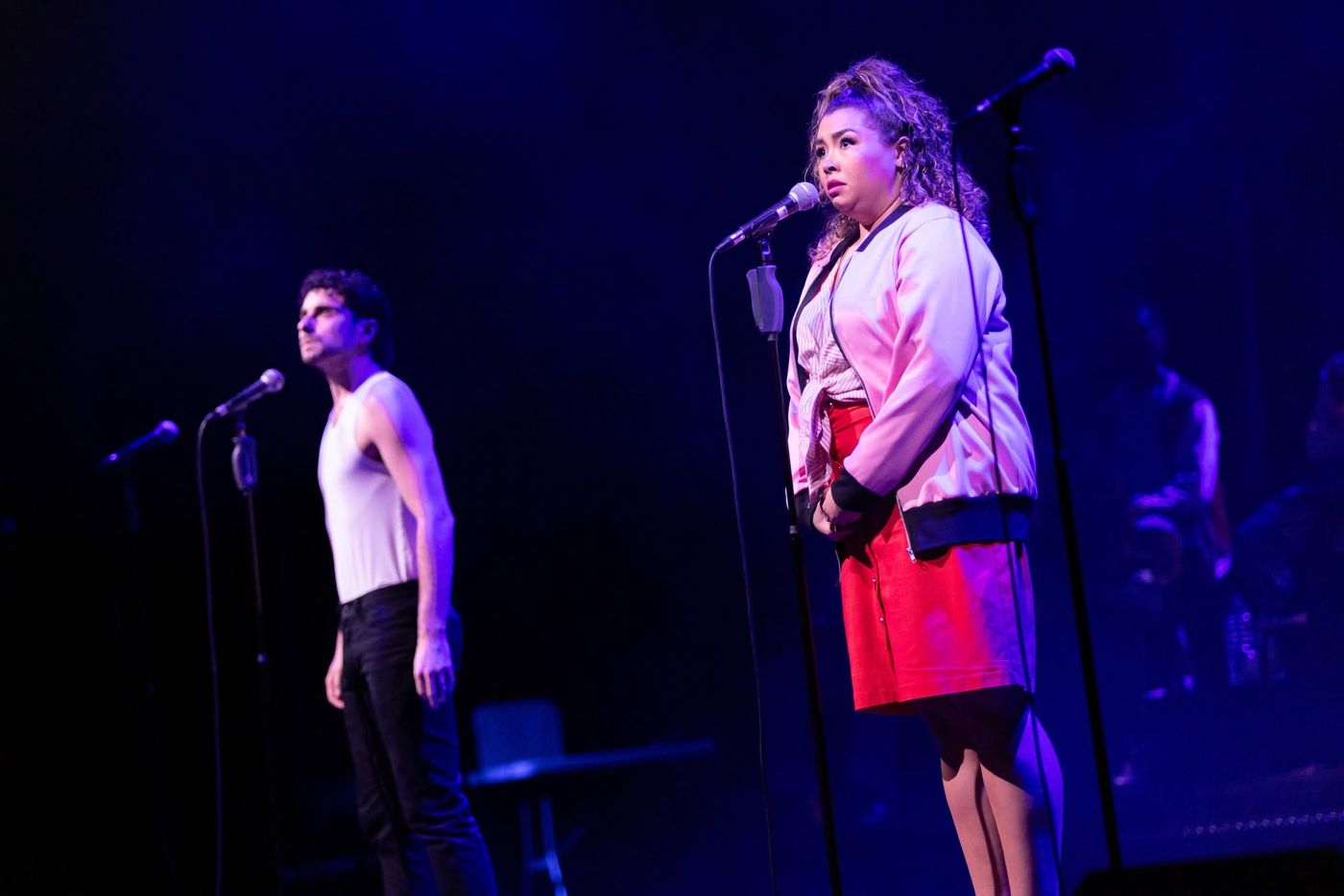 Two performers sharing microphones, one in a red skirt