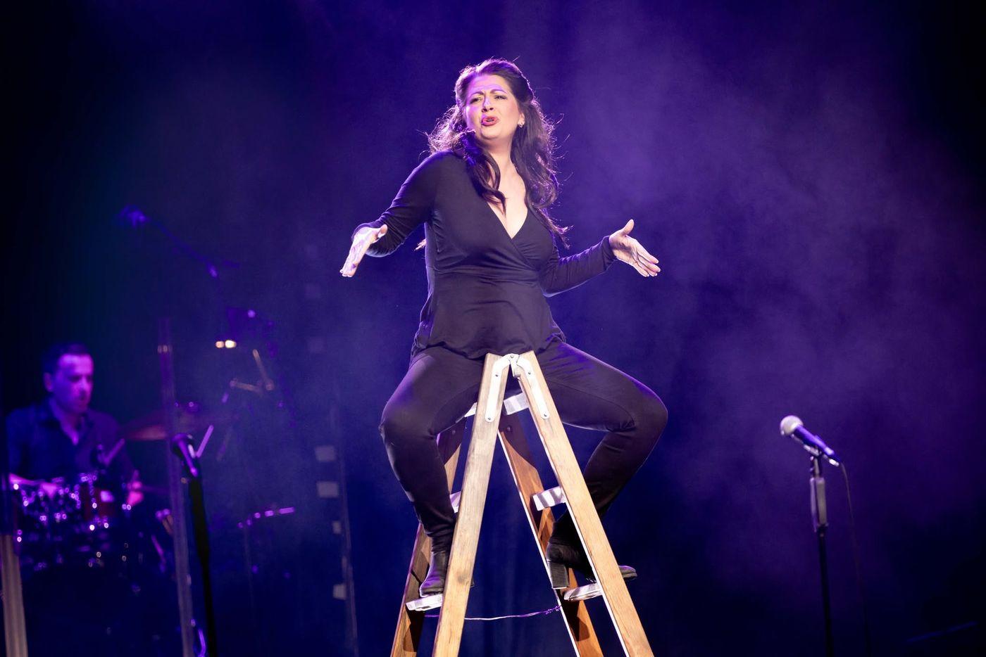 A performer singing from the top of a stepladder in a spotlight