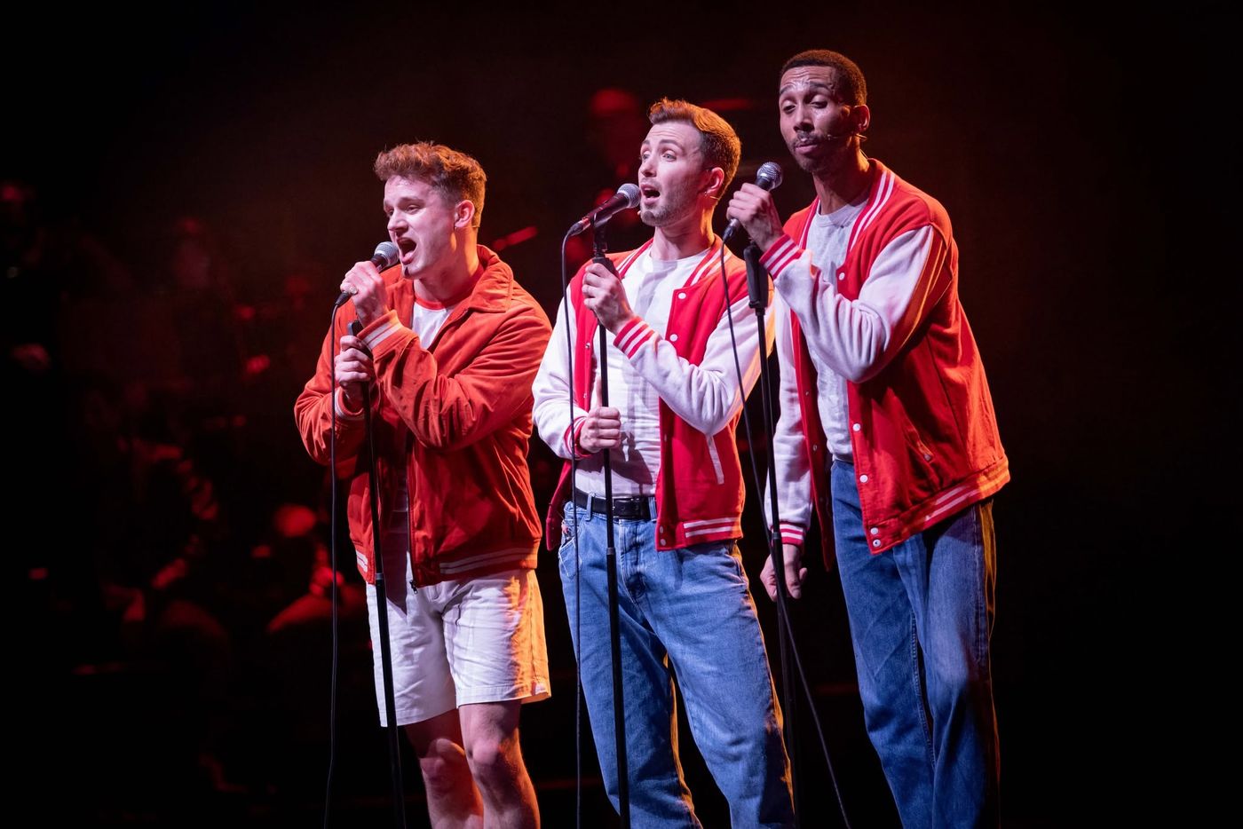 Three performers in red varsity jackets at microphones