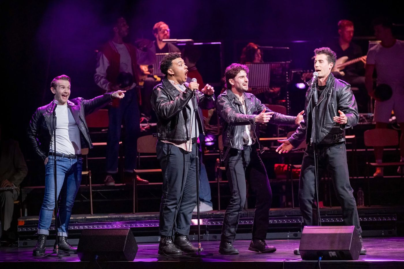 Four performers in leather jackets in front of the band